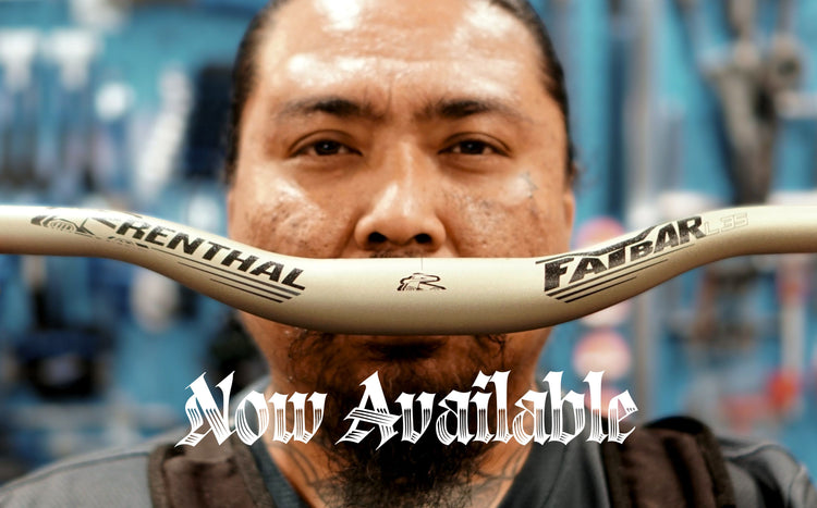 A close-up of a man holding a beige Renthal Fatbar mountain bike handlebar in front of his face, with a workshop background and a 'Now Available' text overlay.