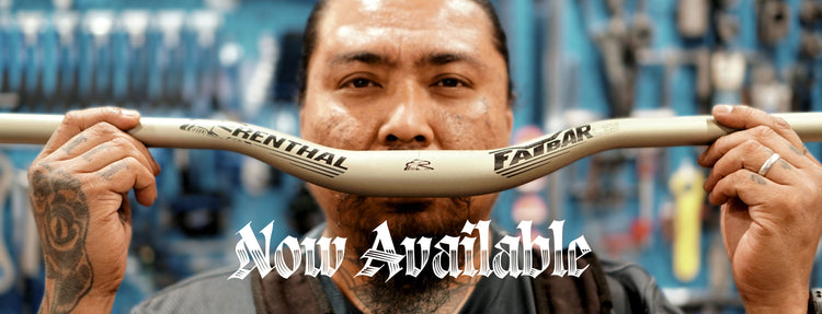 A close-up of a man holding a beige Renthal Fatbar mountain bike handlebar in front of his face, with a workshop background and a 'Now Available' text overlay.