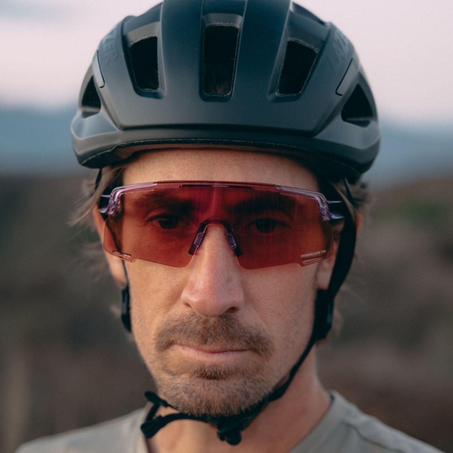Close-up of a cyclist wearing a matte black bike helmet and red-tinted sports sunglasses.