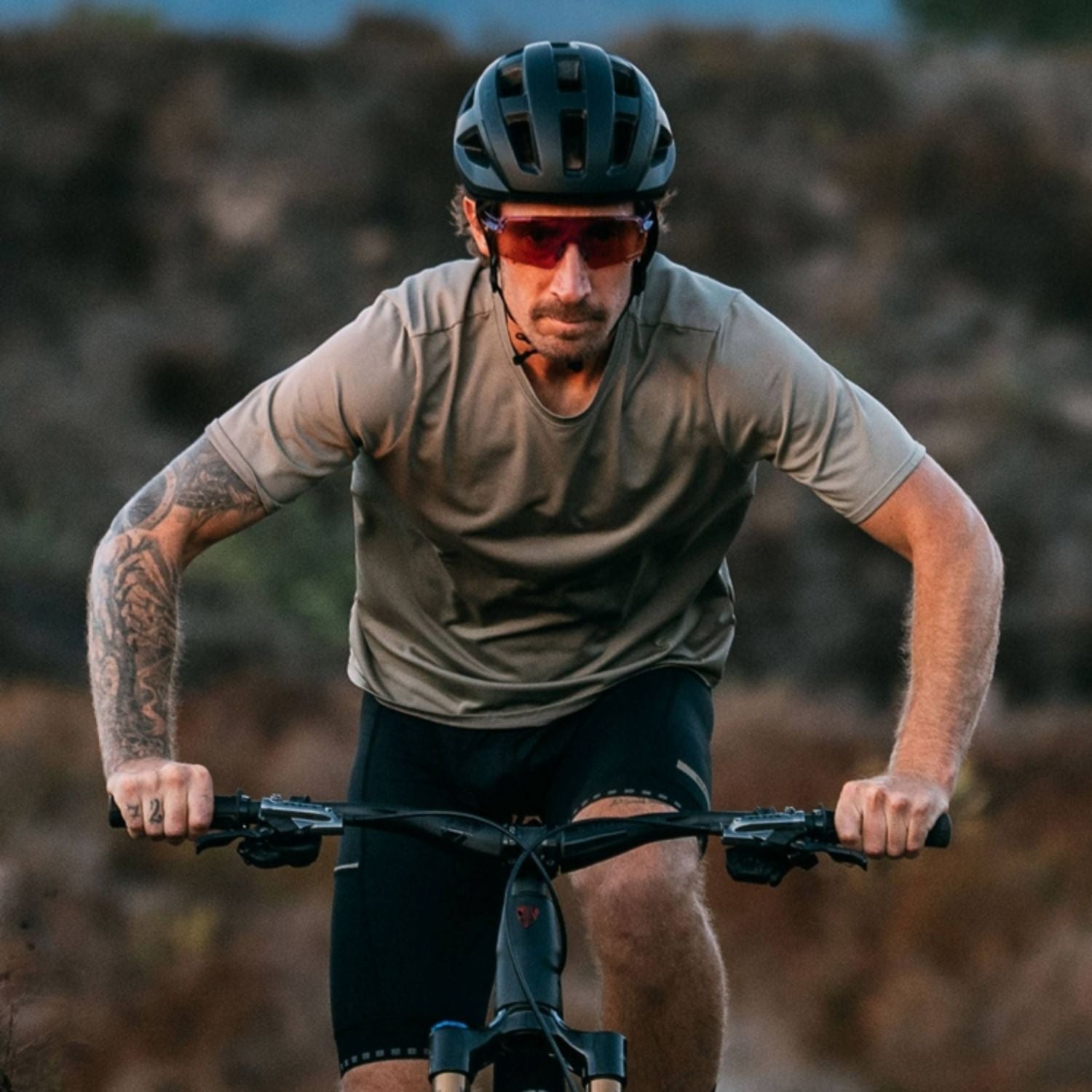Man wearing a cycling helmet and sunglasses riding a mountain bike on a trail